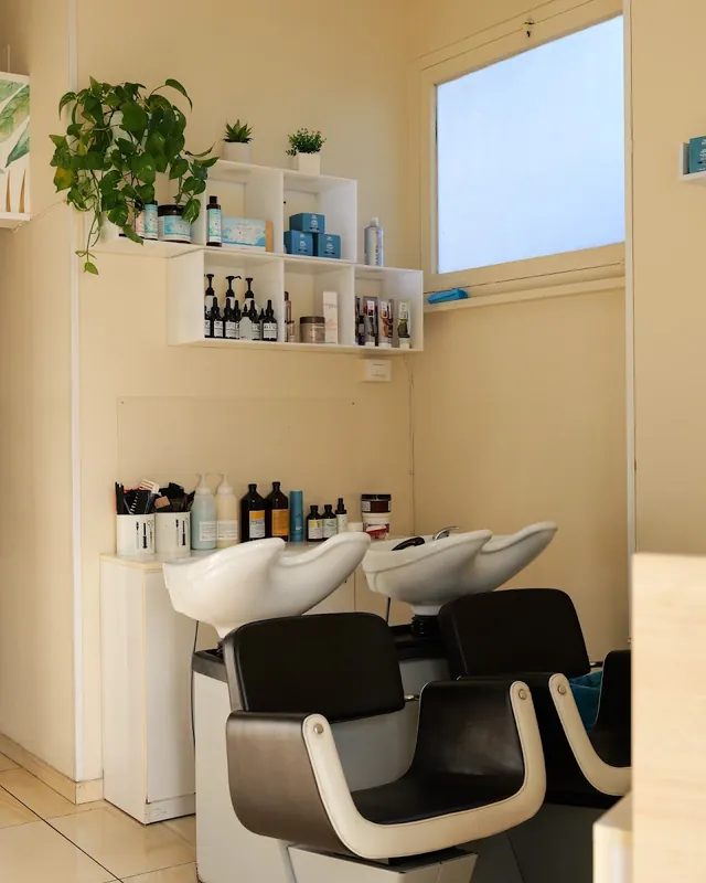 La zona lavaggio con le poltrone bianche e nere e le mensole con piante e prodotti